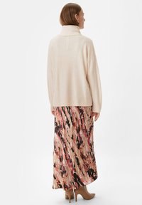 Jasno beżowy sweter z wysokim kołnierzem i prążkowanym dołem, w zestawieniu z zwiewną sukienką w abstrakcyjny różowo-czarny wzór.