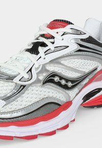 Λευκό, μαύρο και κόκκινο παπούτσι τρεξίματος Saucony με λευκά κορδόνια, υφασματικό πάνω μέρος και παχύ κόκκινο-λευκό πέλμα.