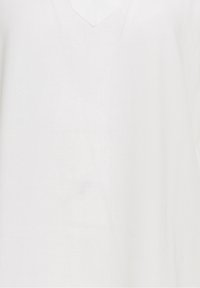 Biała lniana koszula z dekoltem w kształcie litery V i luźnym krojem. Materiał ma lekką teksturę z minimalnie widocznymi szwami.