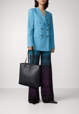 Blazer bleu croisé, pantalon évasé à motifs aux teintes dégradées, sac fourre-tout en cuir noir avec deux longues poignées, texture lisse.