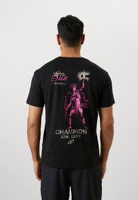 Schwarzes Baumwoll-T-Shirt mit einem großen pinken Grafik eines Statuen, die eine Fackel hält, mit dem Text "Entfessle die Kraft der Sonne" und "CHAMPION ATHL. DEPT." in Silber.