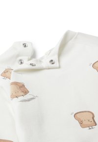 Camisa de algodón blanca con estampados de pan de dibujos animados, con botones a presión en el cuello, textura suave y mangas cortas.