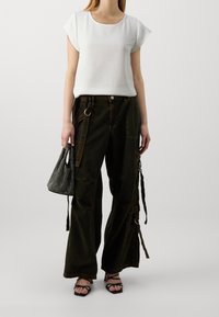 Top bianco a maniche corte abbinato a pantaloni cargo larghi verde scuro con tasche e cinghie. Gli accessori includono una borsa a rete nera e sandali con cinturini.