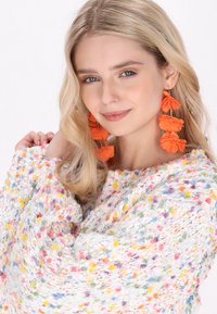 Maglione a maglia multicolore con macchie, maniche lunghe e ampie; abbinato a grandi orecchini a forma di fiore arancione. Design testurizzato e accogliente.