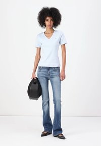 Un tricou bleu deschis cu mânecă scurtă și decolteu în V, asortat cu blugi evazați albaștri. Modelul ține o geantă neagră și poartă pantofi negri cu vârful ascuțit.