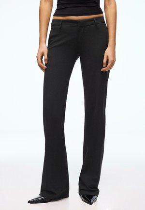 Pantalon noir ajusté avec une coupe droite, doté de poches avant et d'un tissu lisse. Mis en valeur par des chaussures à talons hauts vernies.