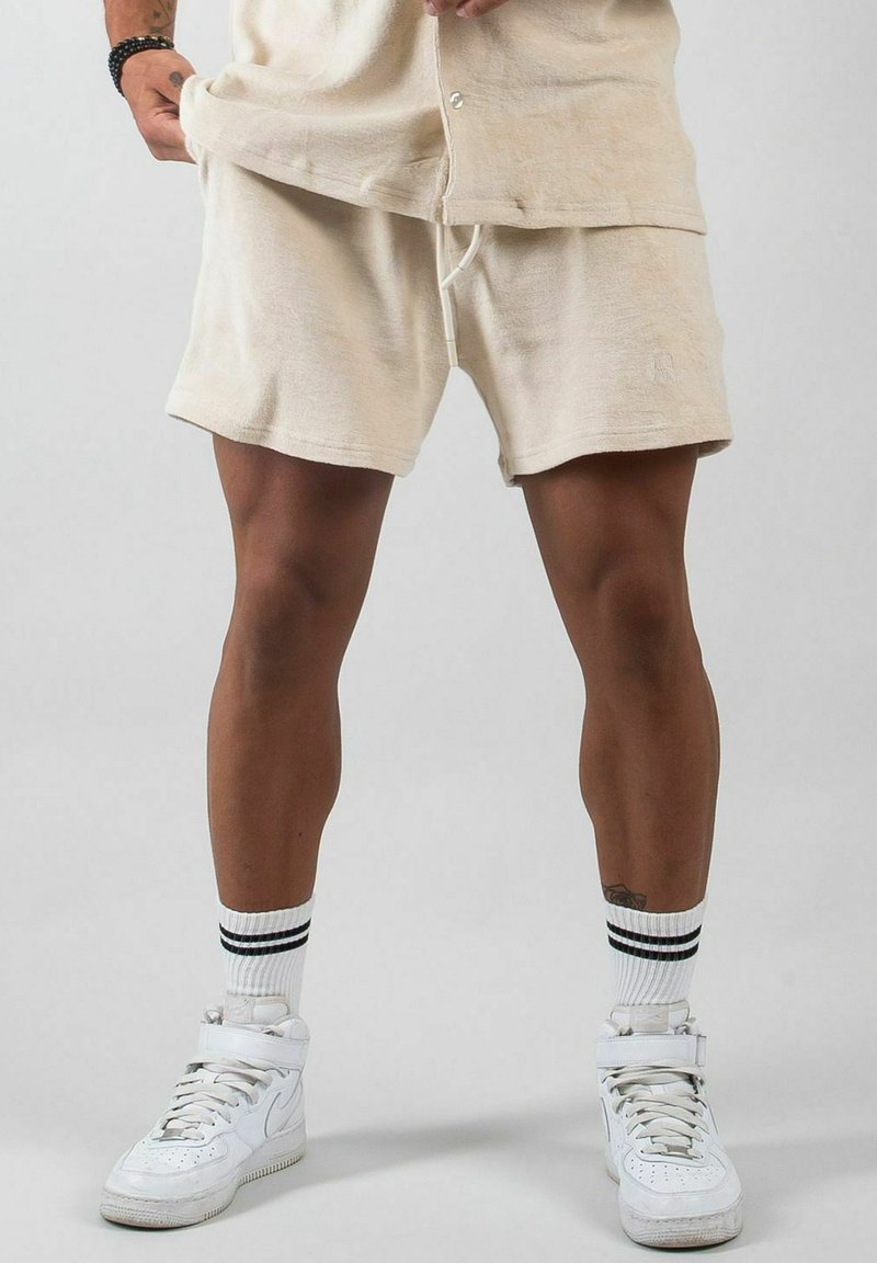 Beige bomullsshorts med dragsko, mjuk struktur och avslappnad passform. Matchas med vita höga sneakers och strumpor med svarta detaljer.