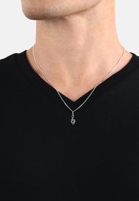 Primo piano di una persona che indossa una maglietta nera a V e una collana d'argento con un pendente a chiave di violino al collo.