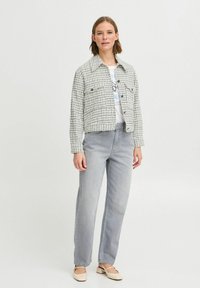 Hvid- og sortternet cropped jakke med knaplukning, parret med lysegrå lige ben jeans og beige flade sko. Enkel design.