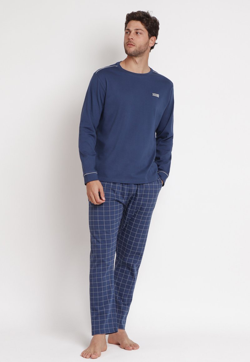 Top a maniche lunghe blu navy abbinato a pantaloni da pigiama a quadri, realizzato in tessuto morbido, con cuciture bianche a contrasto e un dettaglio del logo discreto.