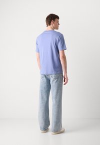 T-shirt de algodão lilás claro com mangas curtas, combinada com umas calças de ganga largas de azul claro. Design simples; ajuste descontraído e textura suave.