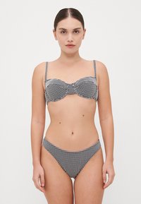 Ensemble de bikini noir et blanc à motifs à carreaux, comprenant un haut balconnet avec des bretelles ajustables et un bas taille basse. Tissu lisse et design ajusté.