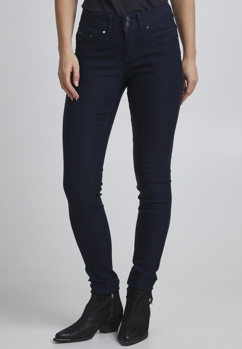 Uske skinny traperice u tamnoplavom denimu s glatkom teksturom. Imaju dva prednja džepa, dva stražnja džepa i zatvaranje na dva gumba u struku.