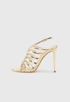 Guldmetallic højhælet sandal med åben tå, der har krydsede stropper og slingback-design. Glat tekstur med en skinnende finish.