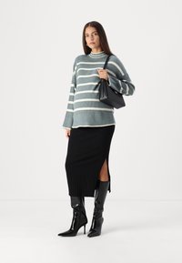 Gestreifter blauer und weißer Pullover, schwarze gerippte Midirock mit seitlichem Schlitz, schwarze spitze knielange Stiefel und eine kleine schwarze Handtasche.