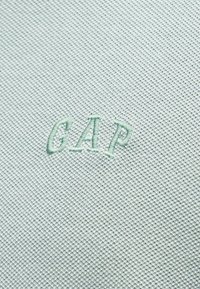 Υφασμα φωτεινού γαλάζιου χρώματος με ανάγλυφη υφή και κεντημένα γράμματα "GAP" στο κέντρο, στο ίδιο χρώμα κλωστής.