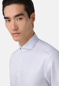 Camisa de vestir blanca con finas rayas azules, de tela suave, con cuello abotonado y un corte estructurado. Presenta una tapeta delantera con botones.