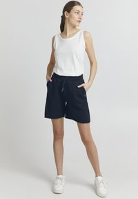 Marineblå bomulds shorts med en rasket kant og en elastisk talje, parret med en hvid ærmeløs top og hvide sneakers.