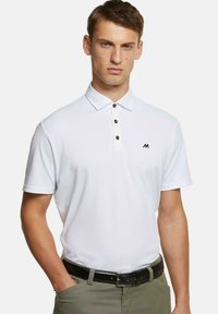 Witte polo met korte mouwen en een kraag, voorzien van een vijfknops sluiting en een klein zwart logo op de borst. Draagt het met olijfgroene broek.