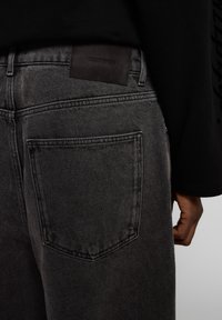 Mustat farkut, joissa on sileä pinta, takatasku ja vyötärön läheisyydessä kohokuvioitu nahkainen etiketti, jossa lukee "EIGHTYFIVE".