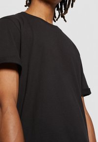 Černé bavlněné tričko s volným střihem, krátkými rukávy a kulatým výstřihem, které vykazuje hladkou texturu a minimalistický design.