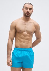 Calções de banho turquesa feitos de material leve com cintura elástica, apresentando uma textura suave e sem padrões ou acessórios visíveis.