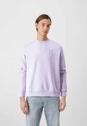 Sweat-shirt lilas clair avec un col ras du cou, des poignets côtelés et une taille côtelée. Présente une lettre "K" en relief discrète sur la poitrine gauche.