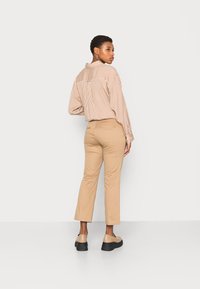 Camisa de botão bege às riscas com um corte relaxado, combinada com calças bege de corte slim e sapatos de plataforma pretos. Fundo simples.