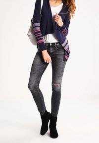 Námořnický kardigan s růžovými a šedými pruhy, bílý tričko, vybledlé šedé džíny a černé kotníkové boty. Hladká látka, přiléhavý střih.