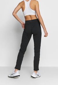 Czarne spodnie sportowe o dopasowanym kroju, wykonane z gładkiego, rozciągliwego materiału. Posiadają zapięcie w pasie oraz wąskie nogawki.