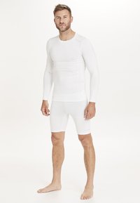 Haut de couche de base sportif blanc à manches longues et shorts de compression blancs, présentant un design ajusté et une texture lisse.