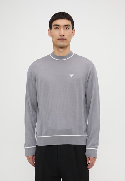 Maglione grigio a maniche lunghe con scollo rotondo, rifiniture bianche e un logo sottile sul petto. Tessuto liscio, vestibilità rilassata, polsini e bordo a coste.