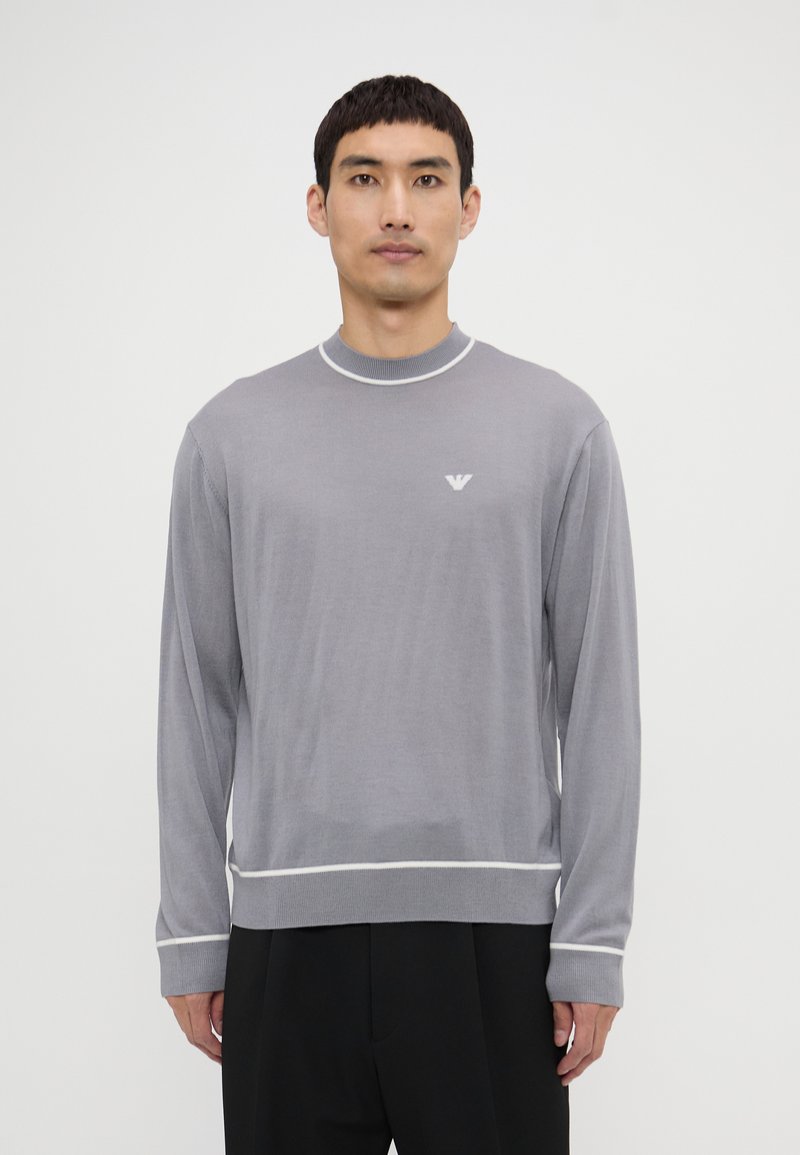 Maglione grigio a maniche lunghe con scollo rotondo, rifiniture bianche e un logo sottile sul petto. Tessuto liscio, vestibilità rilassata, polsini e bordo a coste.