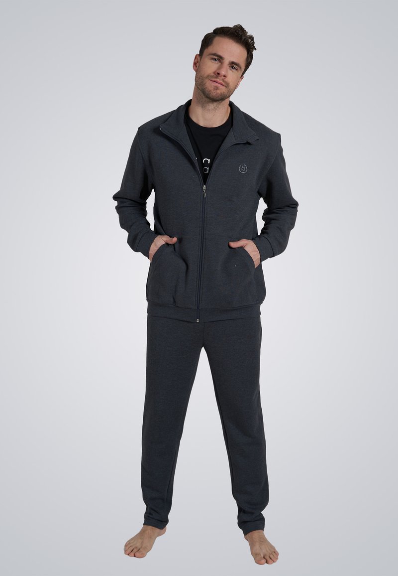 Chaqueta de cremallera gris oscuro con bolsillos laterales y pantalones de chándal a juego, fabricada en un tejido suave, con un logo en el pecho y un corte relajado.