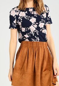 Top navy con fiori rosa, maniche corte, abbinato a una gonna in suede marrone con pence e tasche laterali.