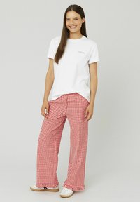 T-shirt en coton blanc avec du texte bleu, associé à un pantalon large en vichy rouge. Les chaussures ont une base blanche avec une semelle marron clair.