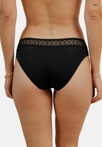 Sous-vêtements noirs avec une taille en dentelle. Le tissu est doux et extensible, présentant un design échancré avec des bords festonnés sur la dentelle.