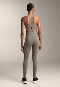 Olivnozeleni športni modrček s krvozadnjimi naramnicami in izrezanimi detajli, v kombinaciji z visokim pasom legicami, oboje izdelano iz raztegljivega materiala.