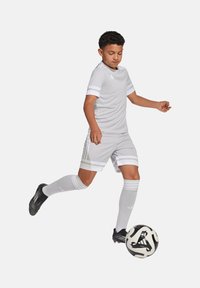 Uniforme de football gris clair avec des accents blancs, à manches courtes et chaussettes à mi-mollet. Un ballon de football noir et blanc est en jeu.
