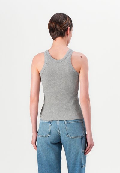 Top din bumbac gri, cu dungă, cu un design ajustat și bretele late, asortat cu blugi din denim albastru deschis. Cusăturile expuse și buzunarele sunt vizibile.