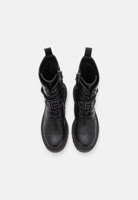 Botas de piel negra hasta el tobillo con punta redonda, cordones en la parte frontal y cremalleras laterales. Estilizadas con un detalle de logo texturizado y suelas de goma resistentes.