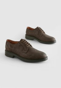 Brown suede dress shoes with a rounded toe, five eyelet lace-up design, and a textured surface. Black rubber sole with a slight heel.