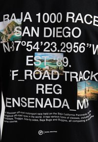 Černé tričko s bílým textem o závodu Baja 1000, s malými obrázky krajin a detaily o události a lokalitě.
