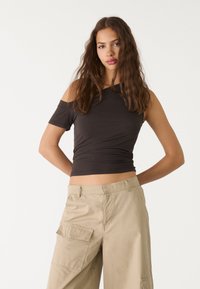 Tmavohnedý, off-the-shoulder top vyrobený z jemného materiálu, priliehavého strihu. Nosí sa s svetlo béžovými cargo nohavicami s bočnými vreckami.