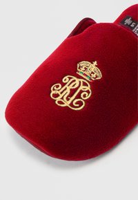 Κόκκινη βελούδινη παντόφλα με χρυσό στέμμα και περίτεχνη κεντημένη μέρα "RP". Μαλακή υφή με καμπύλο σχήμα και ανοιχτό π�ίσω σχέδιο.