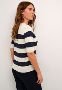 Strikket kortermet topp med marineblå og hvite horisontale striper. Stoffet ser teksturert ut med en avslappet passform og ribbestrikket halslinning.