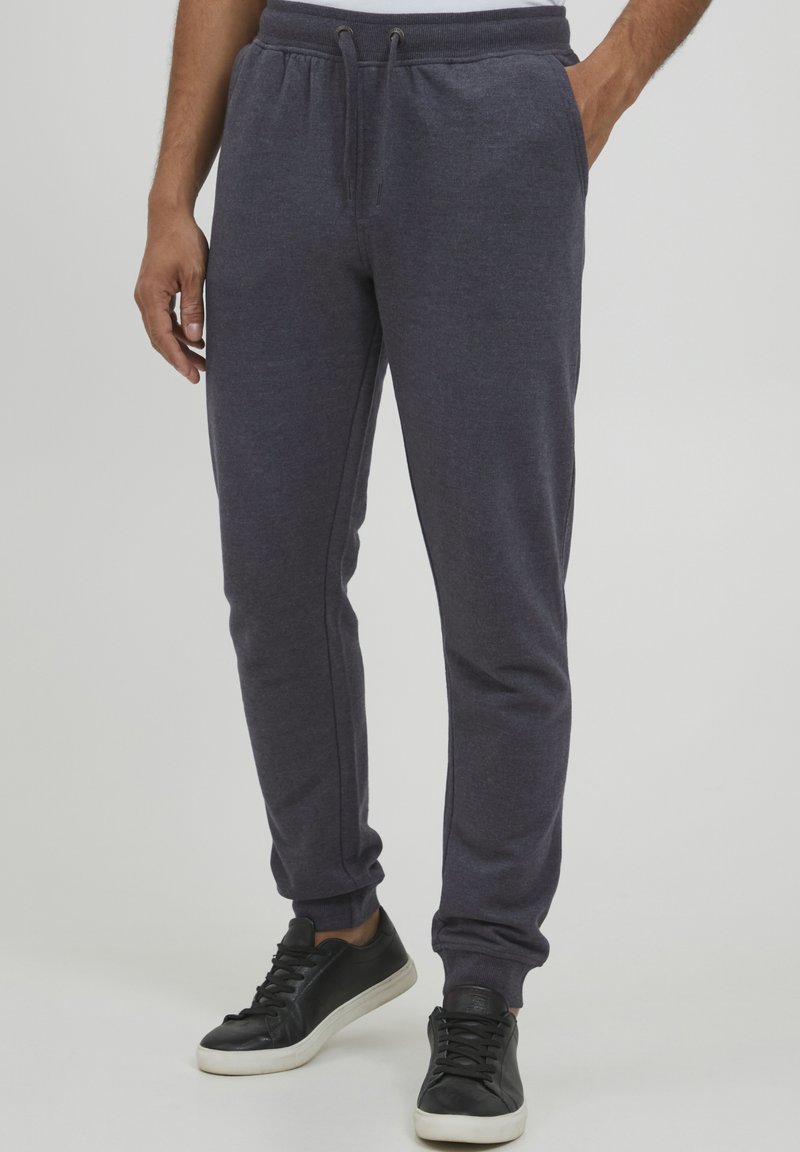 Dark gray athletic joggers with an elastic waistband, adjustable drawstring, side pockets, and tapered legs, paired with black sneakers.