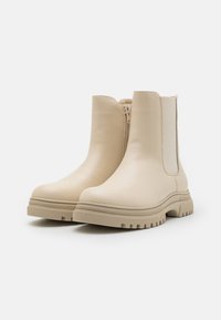 Bottines beiges en cuir lisse avec des panneaux latéraux élastiques et une semelle en caoutchouc texturé dotée d'un bord strié.