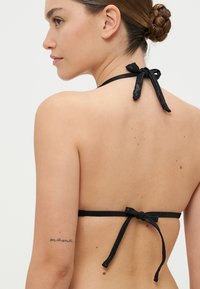 Crni bikini top s tankim, vezanim trakama. Glatka tkanina s minimalističkim dizajnom. Uključuje vezivanje na leđima za prilagodljivu veličinu.