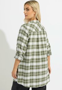 Zielono-biała koszula flanelowa w kratę z zaokrąglonym dołem, zapinanymi rękawami i plecakiem z plisą, uszyta z miękkiego materiału.